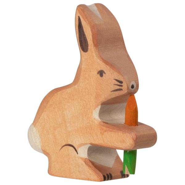 Wooden rabbit figurine holding a carrot on a white background