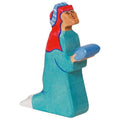 Wooden figurine of a person wearing a blue outfit and red head covering on a white background