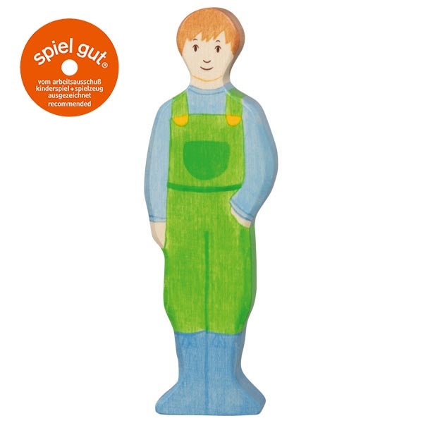 Wooden toy figure of a boy wearing green overalls on a white background