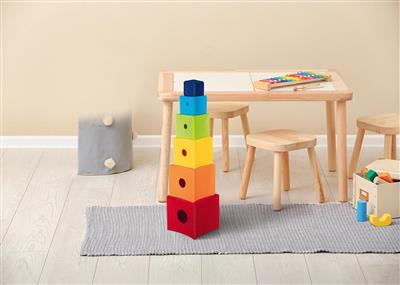 Colorful stacking blocks on a rug in a room with a wooden table and chairs.